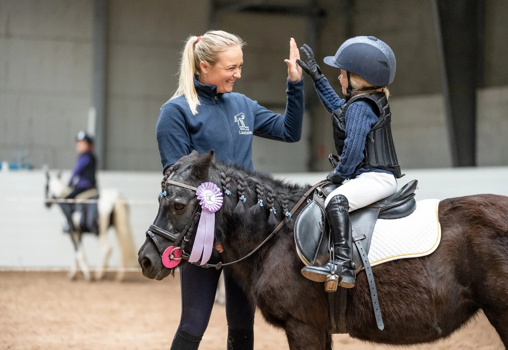 Rideskolelærer gir high-five til jente på en dekorert ponni.